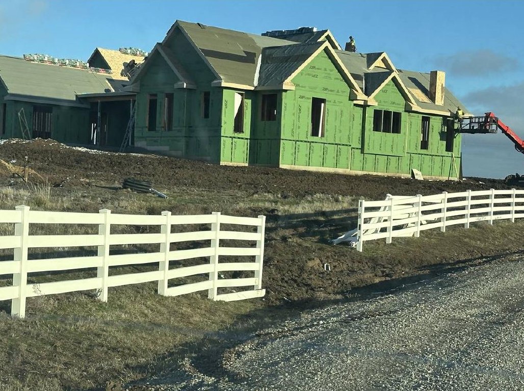 Custom home with green exterior sheathing and white fencing during construction