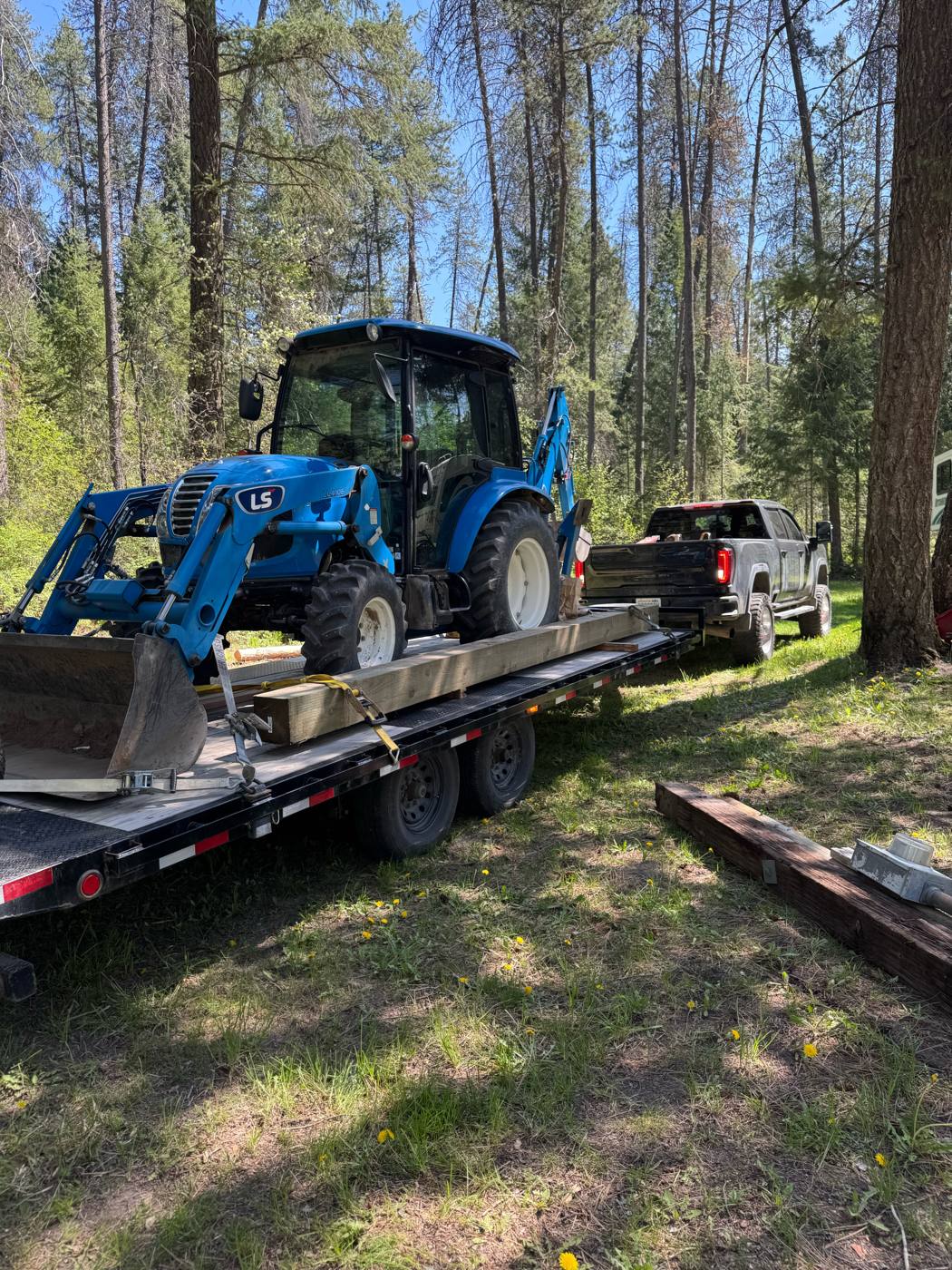 Our LS backhoe on a tilt trailer behind the truck at a wooded job site