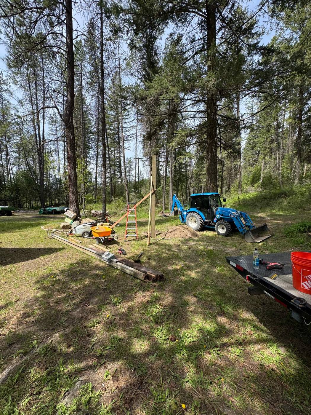 Backhoe and trailer at a wooded property while setting a new electrical service pole and trenching